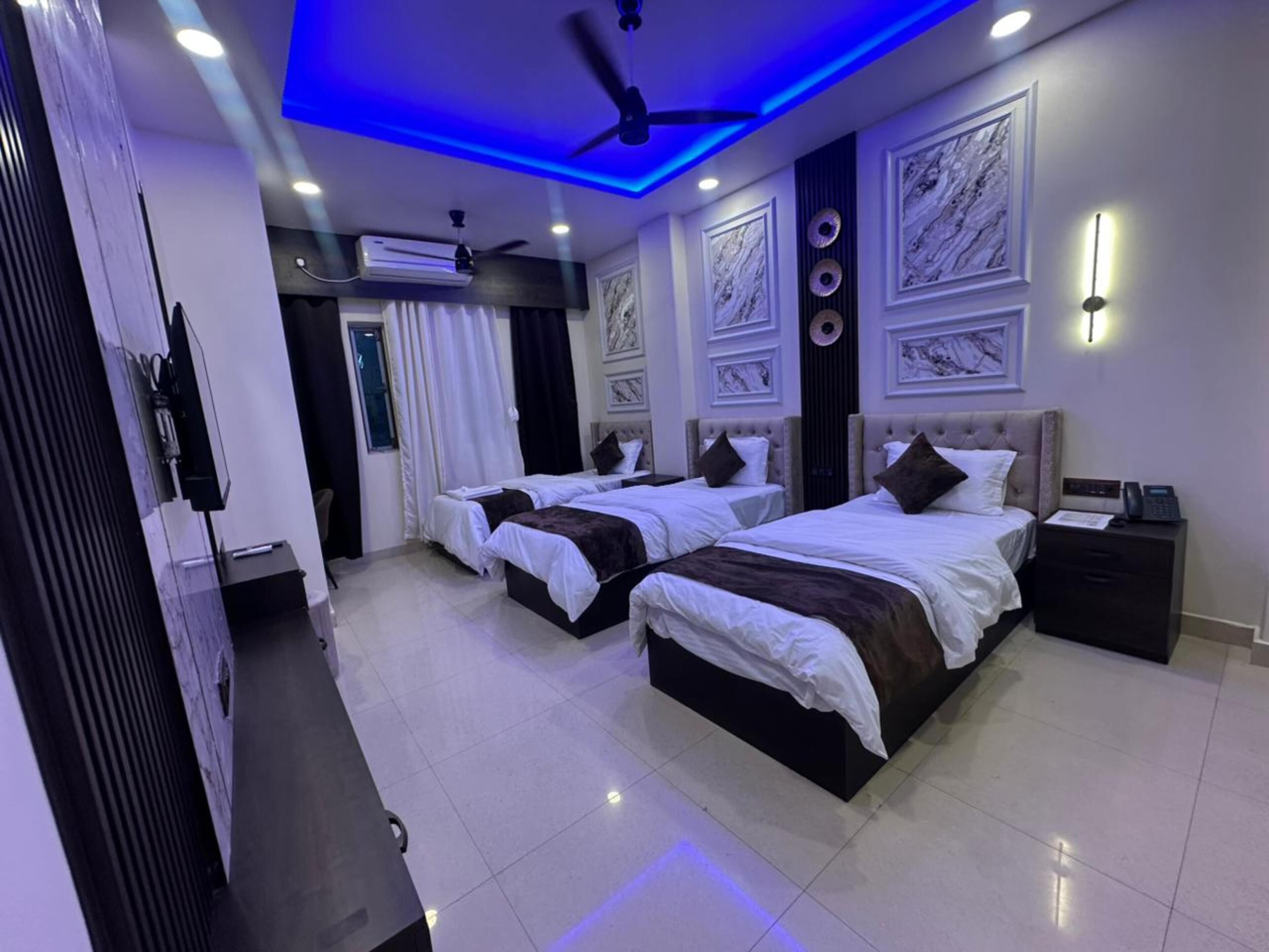 A hotel room with two beds, a ceiling fan, an air conditioning unit, and a telephone on a bedside table.
