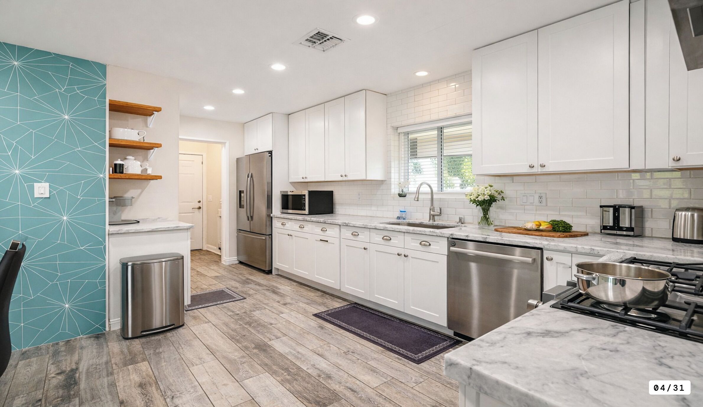 A modern kitchen with white cabinets, stainless steel appliances, and a marble countertop.