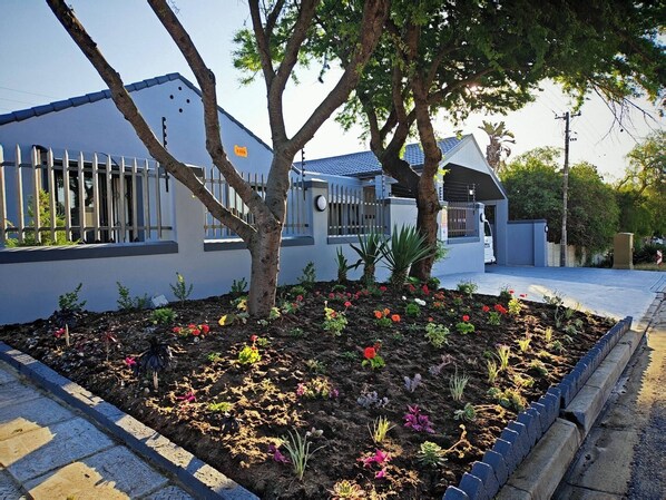A modern building with a white exterior, a gated entrance, and a landscaped garden with various plants and flowers. - Stylish Studio Room with Shared Pool Near Table View Beach (Cape Town)