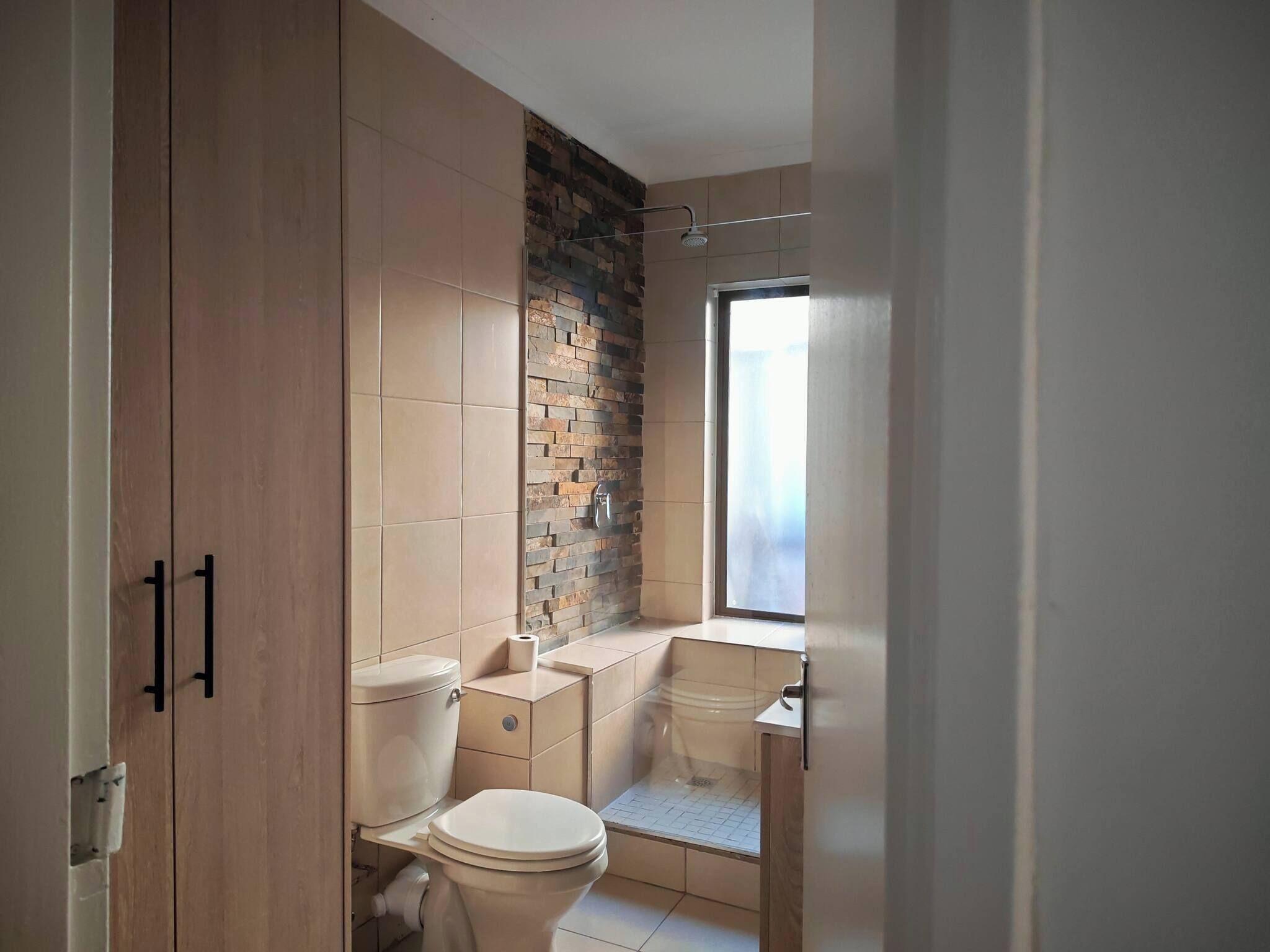 A bathroom with a toilet, a shower, and a window.