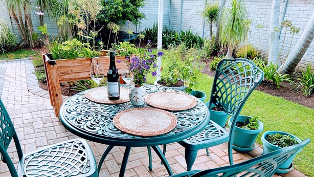 Une terrasse avec une table ronde et des chaises, une bouteille de vin et des plantes en pot.