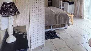 A bedroom with a bed, a bedside table with a lamp, a wardrobe, a desk with a chair, and a bathroom visible through an open door.