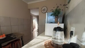 A kitchen with a white countertop, a black coffee maker, a potted plant, and a bowl of oranges.