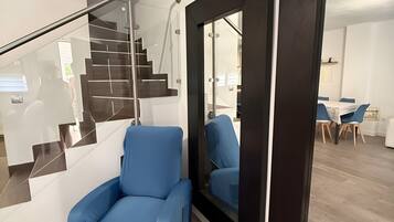 Un interior moderno con una escalera, un sillón azul y un comedor con mesa y sillas.