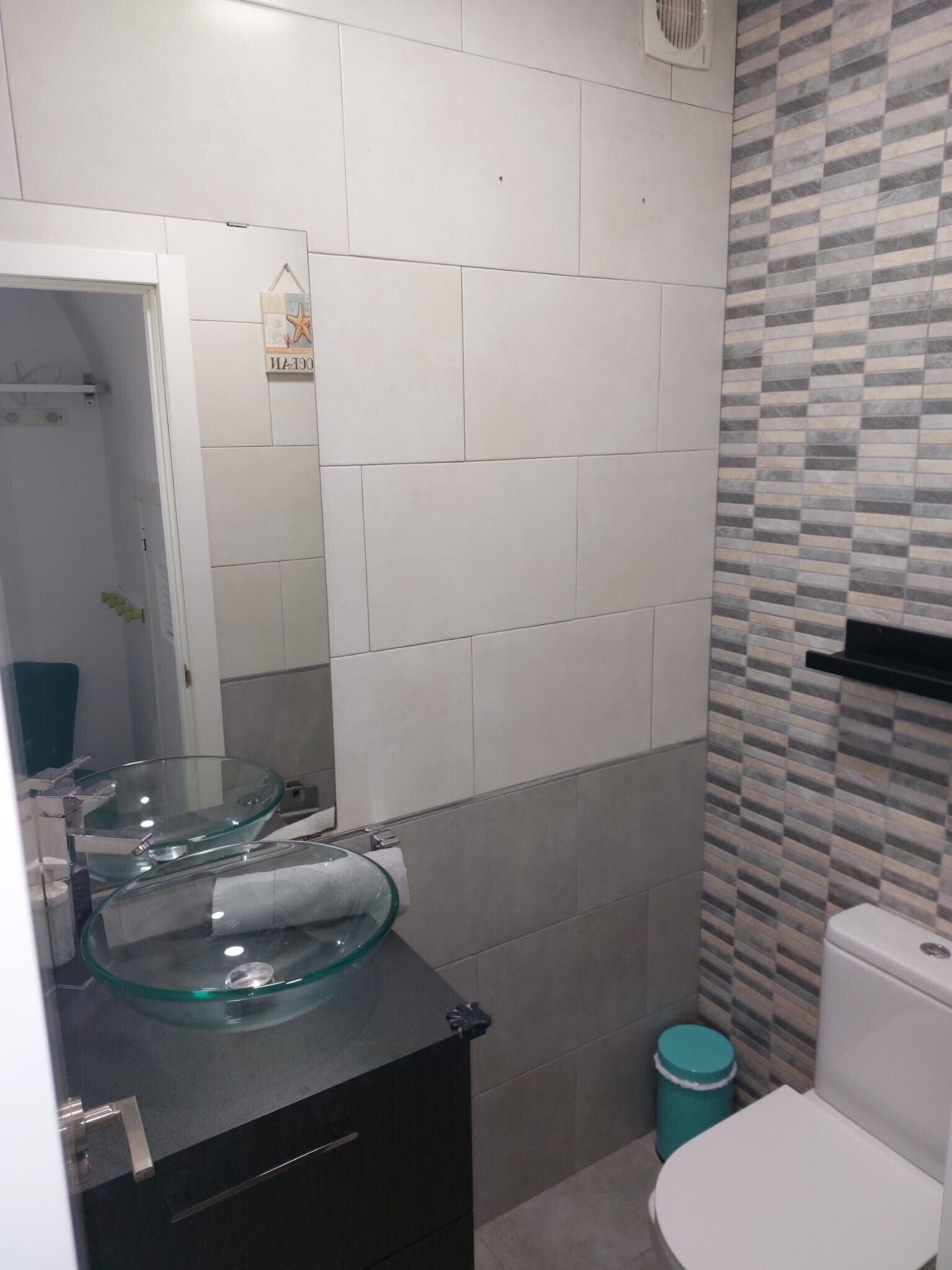 Une salle de bain avec un lavabo en forme de bol en verre, des toilettes blanches et une poubelle.