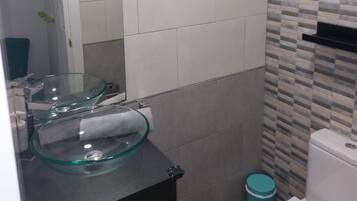 Une salle de bain avec un lavabo en forme de bol en verre, des toilettes blanches et une poubelle.