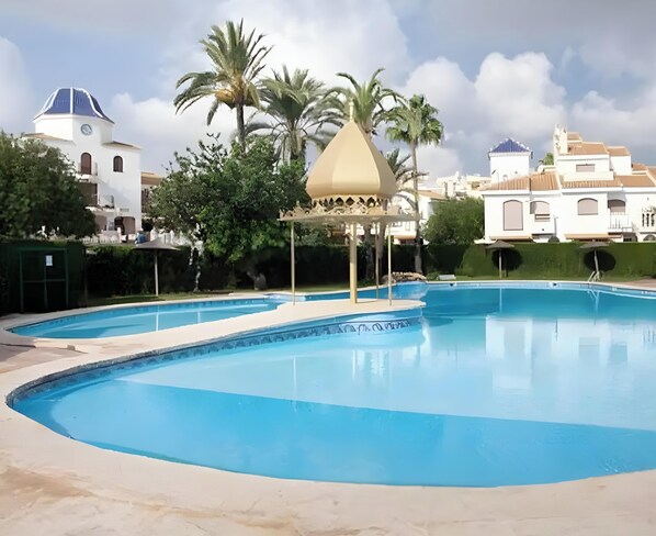 Una piscina con un pabellón, palmeras y un edificio blanco con cúpula al fondo.