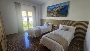 A hotel room with two beds, a painting of a coastal town, a balcony with curtains, and a tiled floor. - Country House 'Villam Rodericus Nicolaus' with Private Pool, Wi-Fi and Air Conditioning (Lantejuela)