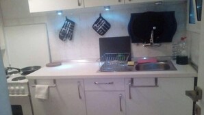 Una cocina compacta con gabinetes blancos, un lavamanos de acero inoxidable y una estufa.