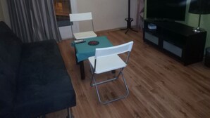 Una sala de estar con un sofá, una mesa de comedor con sillas, un televisor y una lámpara de pie.