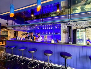 A bar area with a blue-lit counter, multiple stools, and a variety of bottles and glasses. - Relaxing Suite with Balcony and Patong City View (Tambon Patong)