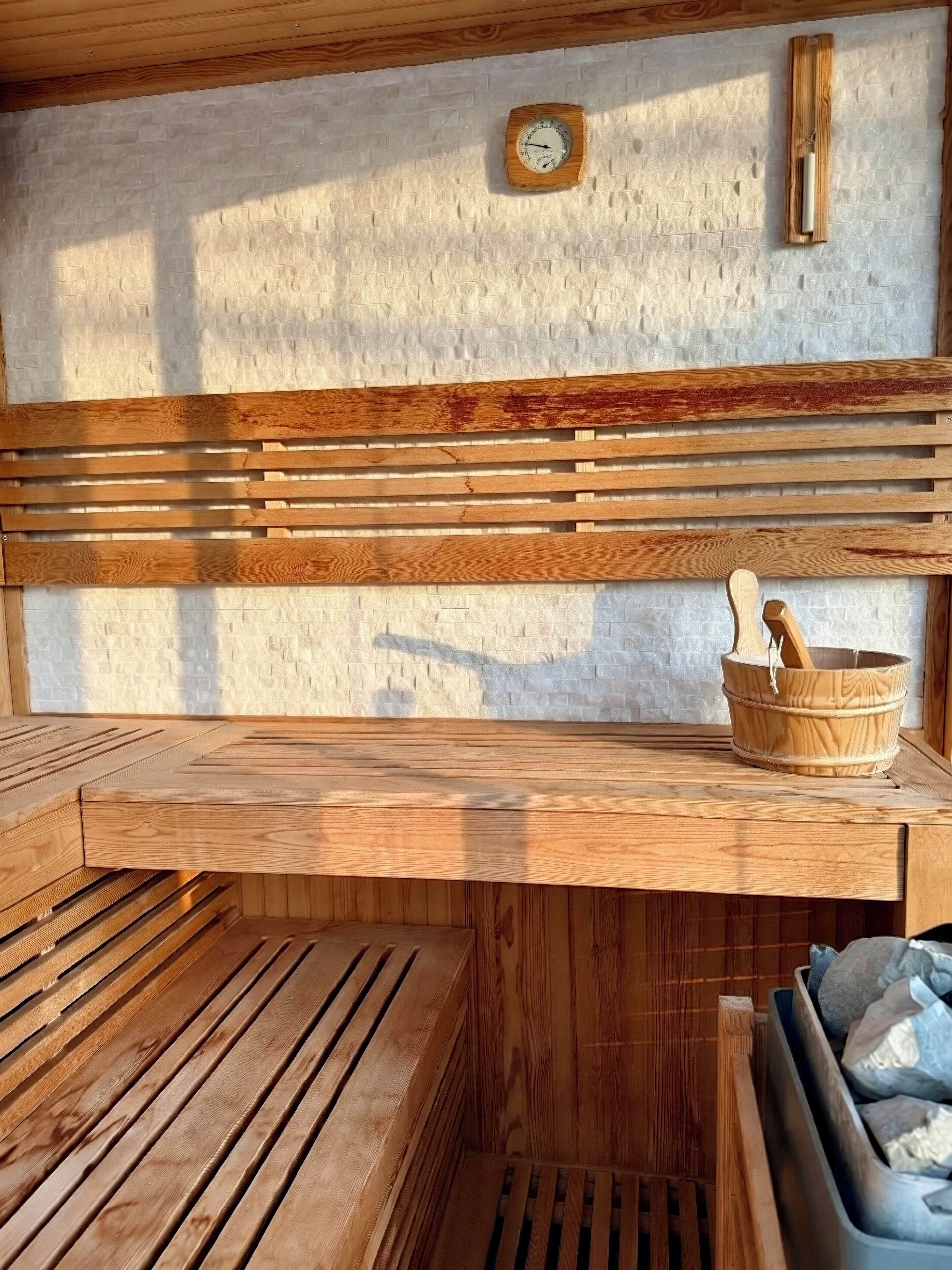 Una sauna con panche di legno, una sveglia a muro in legno e un catino di legno con una schiumarola.