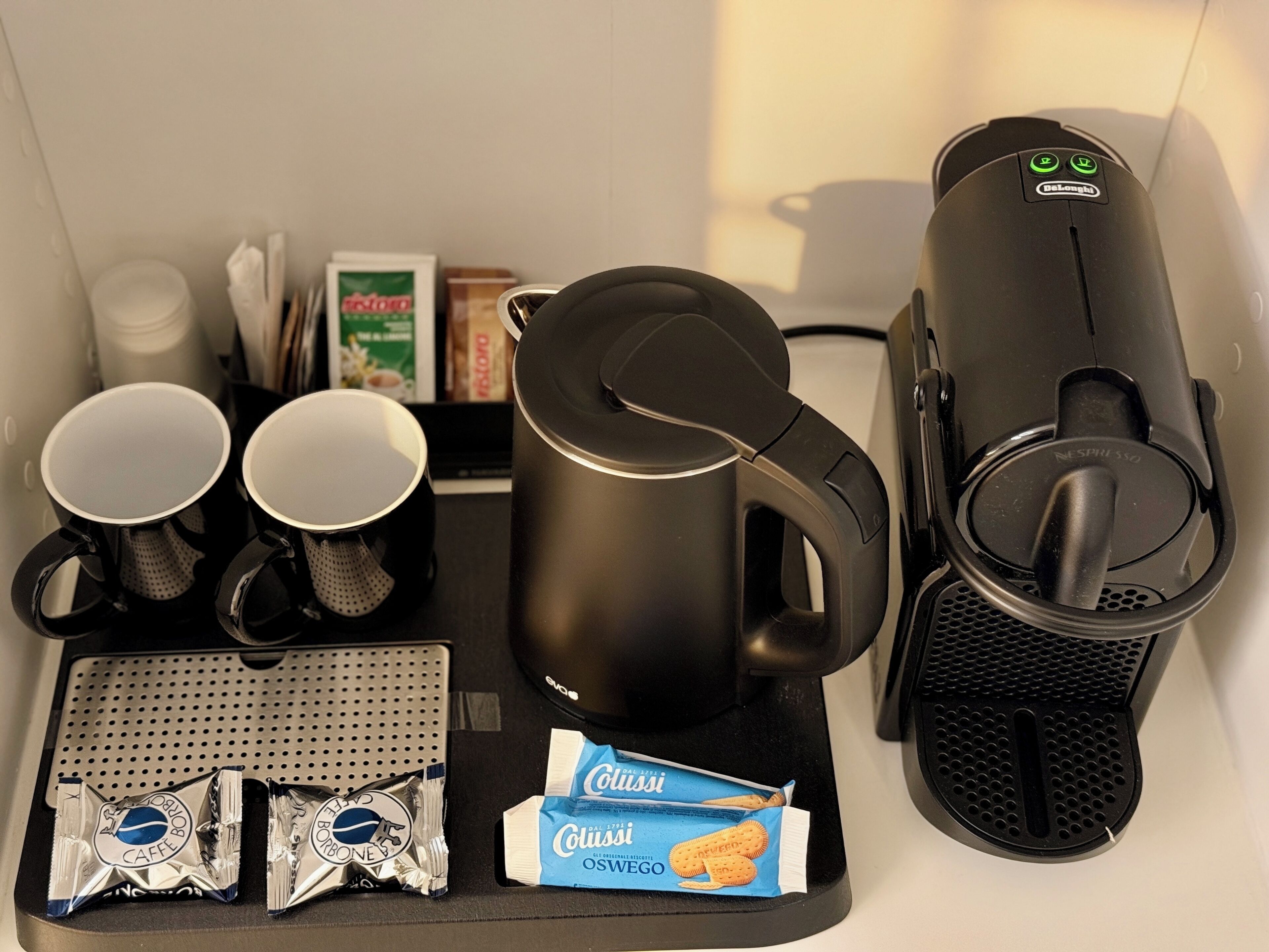 Une machine à café, deux tasses, une bouilloire, un support pour dosettes de café et une boîte de biscuits secs.