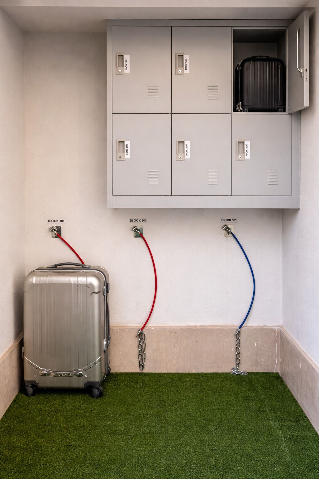 Een kamer met een grijze wand, een grijze opbergunit met vakken, en een zilveren koffer met rode en blauwe kabels.