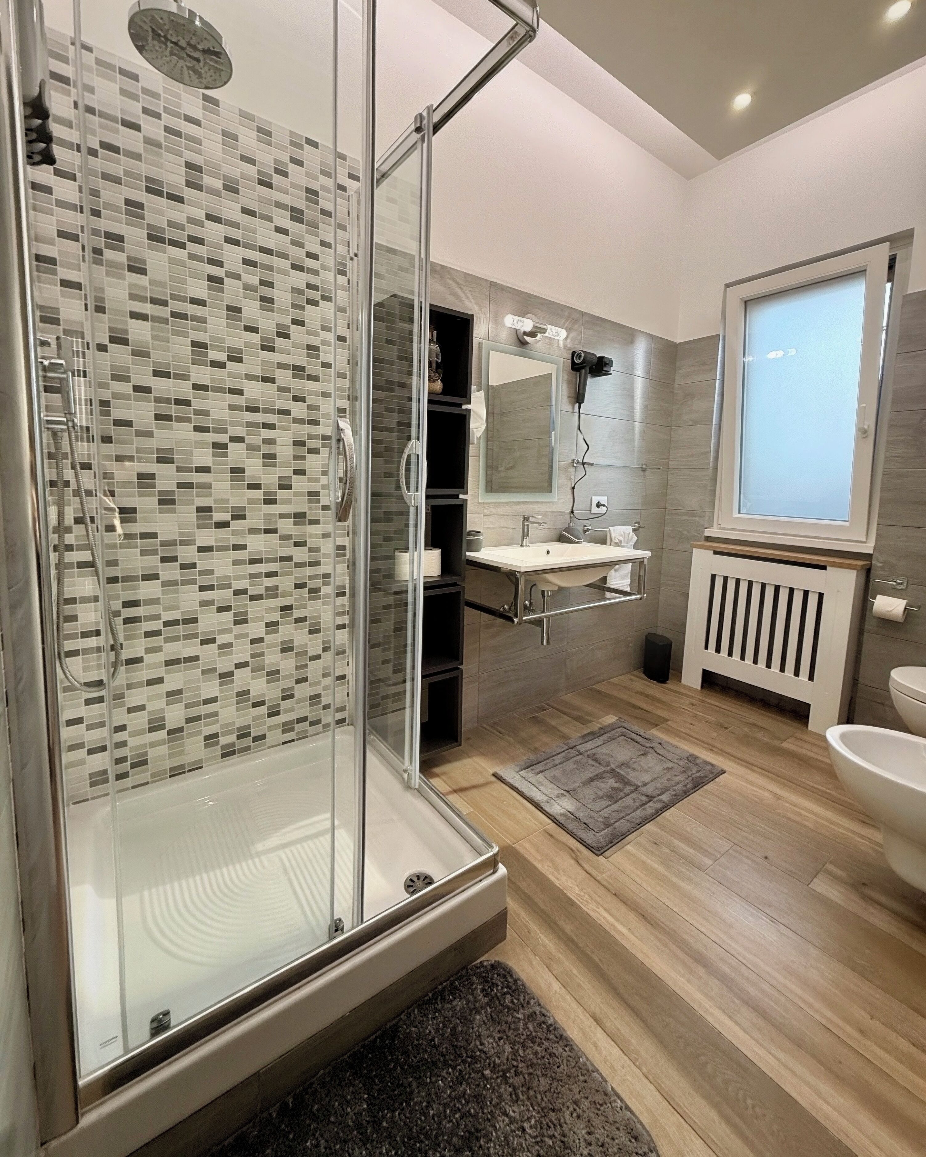 Een moderne badkamer met een douchecabine van glas, een wastafel, een spiegel en een radiator.