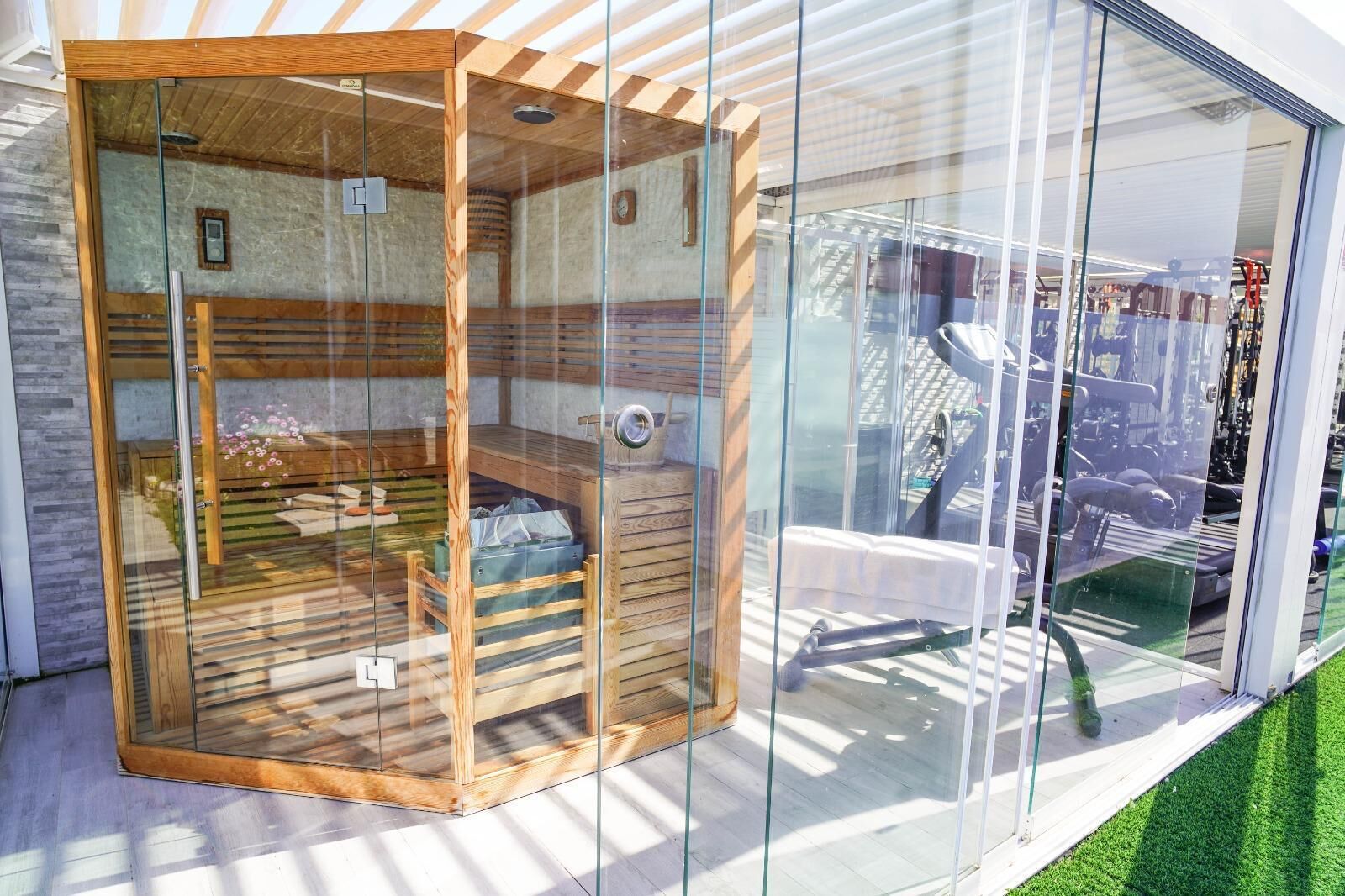 A modern glass-enclosed sauna with wooden benches and a door.