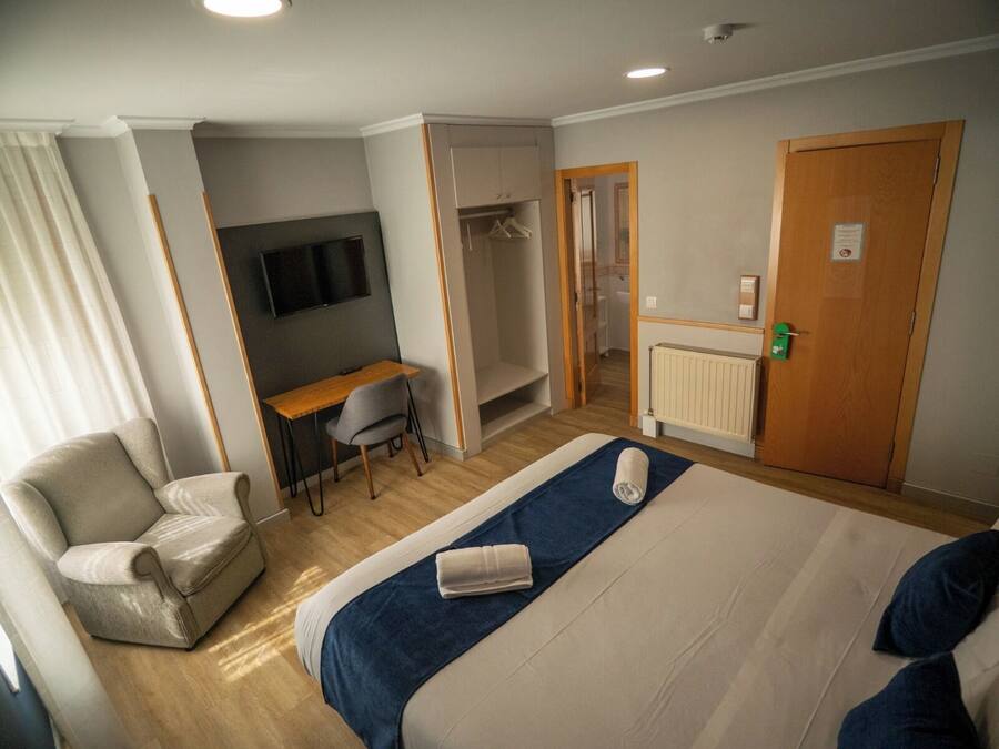 Quarto de hotel com cama, escrivaninha, cadeira, televisão, guarda-roupa e banheiro.