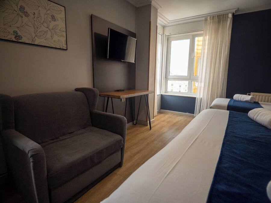 Una habitación de hotel con sofá, cama con colcha azul, escritorio pequeño y televisor de pantalla plana, además de ventana con cortinas.