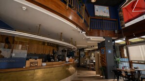 A hotel lobby with a reception desk, a staircase, and a dining area.