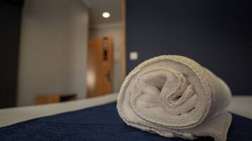 Ein gerolltes, weißes Handtuch auf einer dunkelblauen Hotelbettdecke.