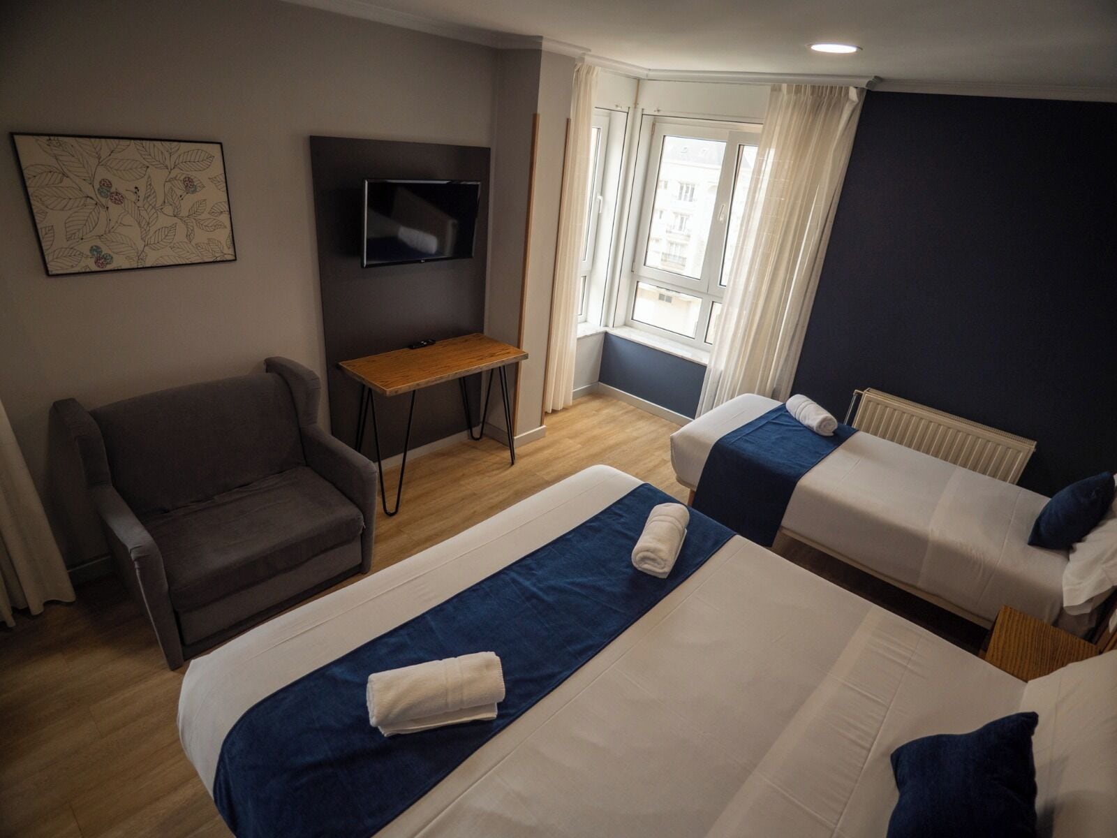 Habitación de hotel con dos camas, un sofá, un televisor y una ventana con cortinas.