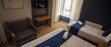 A hotel room with two beds, a sofa, a TV, and a window with curtains.