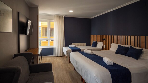 A hotel room with two beds, a desk, a chair, and a TV.