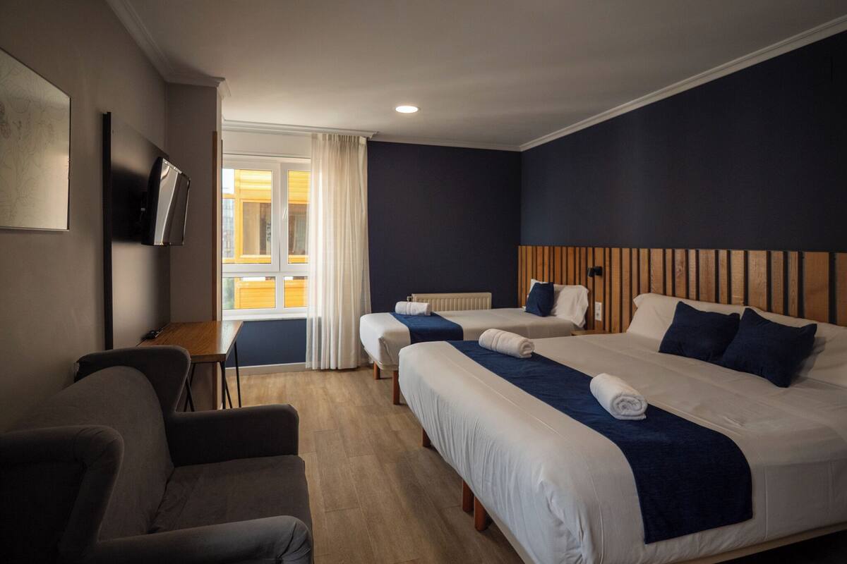 A hotel room with two beds, a desk, a chair, and a TV.