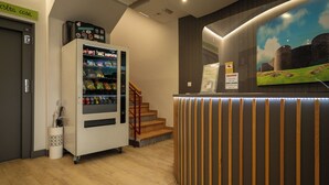 A reception area with a vending machine, a staircase, and a wall-mounted display.