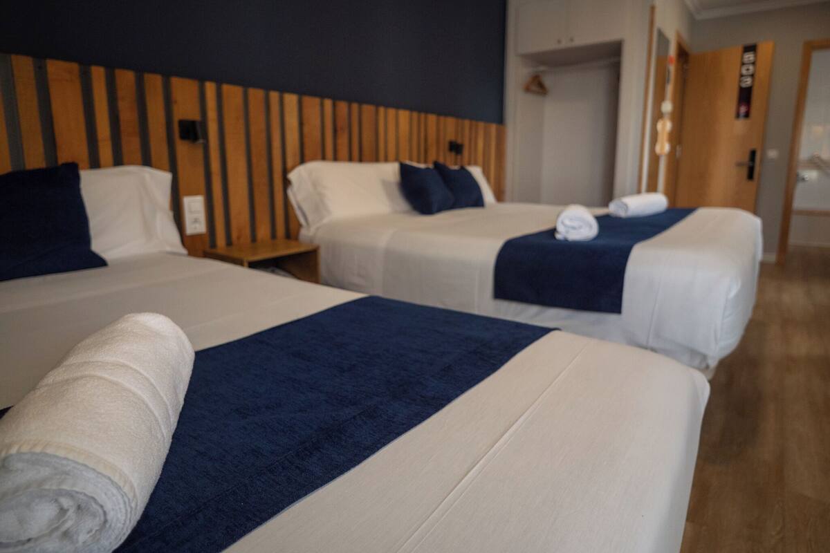 A hotel room with three beds, wooden headboard panels, and a wooden floor.