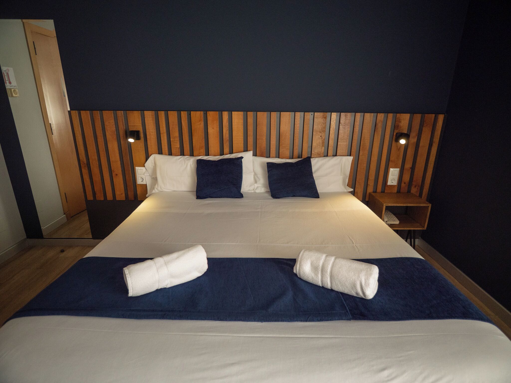 A hotel room with a large bed, wooden headboard, two bedside tables, and a nightstand.