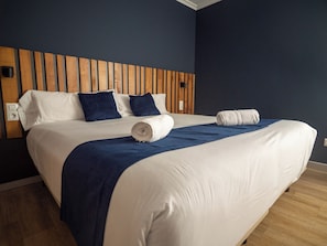 A hotel room with a wooden headboard, a large bed with white bedding, two blue pillows, and a blue throw blanket.