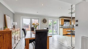 A dining area with a table, chairs, and a vase of flowers. There is a kitchen visible through an open door. - Charming 3-Bedroom House in Radcliffe, Manchester (Radcliffe)