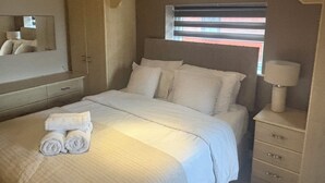 A bedroom with a bed, a bedside lamp, a mirror, and a window with blinds. - Charming 3-Bedroom House in Radcliffe, Manchester (Radcliffe)