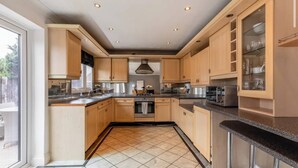 A modern kitchen with wooden cabinets, a central island, and built-in appliances. - Charming 3-Bedroom House in Radcliffe, Manchester (Radcliffe)