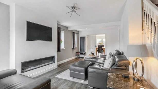A modern living room with a fireplace, leather sofa, and a TV mounted on the wall. - Charming 3-Bedroom House in Radcliffe, Manchester (Radcliffe)