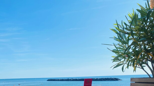 Une table bleue est placée à l’extérieur, avec deux verres de bière et un téléphone intelligent dessus. On aperçoit une plage et une formation rocheuse en arrière-plan.