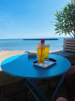 A table with two glasses of beer and a smartphone on a blue table outdoors with a beach and rocky outcrop in the background. - Mezzanine studio in a cocooning location! (Agde)