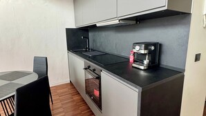 Una cocina compacta con horno integrado, cafetera y zona de comedor con mesa y sillas.