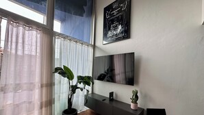 Una sala de estar moderna con un ventanal grande, una planta en maceta, un televisor de pantalla plana y una consola minimalista.