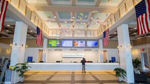 Empfangsbereich des Grand Palms Resort mit einem zentralen Empfangstresen, amerikanischen Flaggen und digitalen Bildschirmen, die Informationen zeigen.