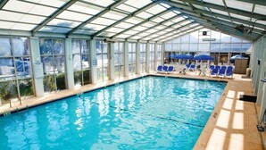 Ein überdachter, heller Innenpool mit Panoramafenstern, blauen Stühlen.