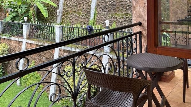 A balcony with a wicker chair and table, a stone wall, and a view of banana plants.