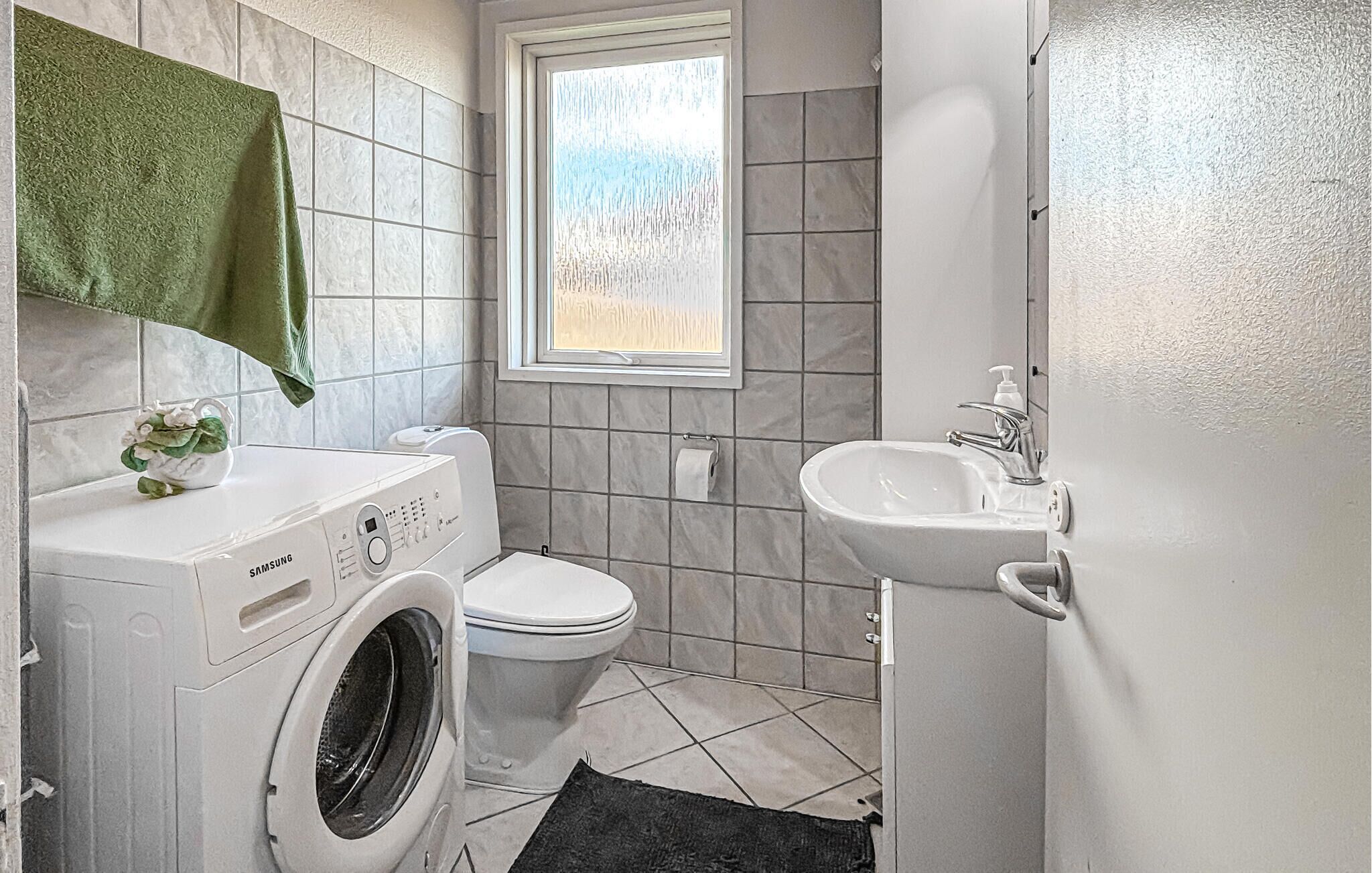 A compact bathroom with a washing machine, toilet, and sink.