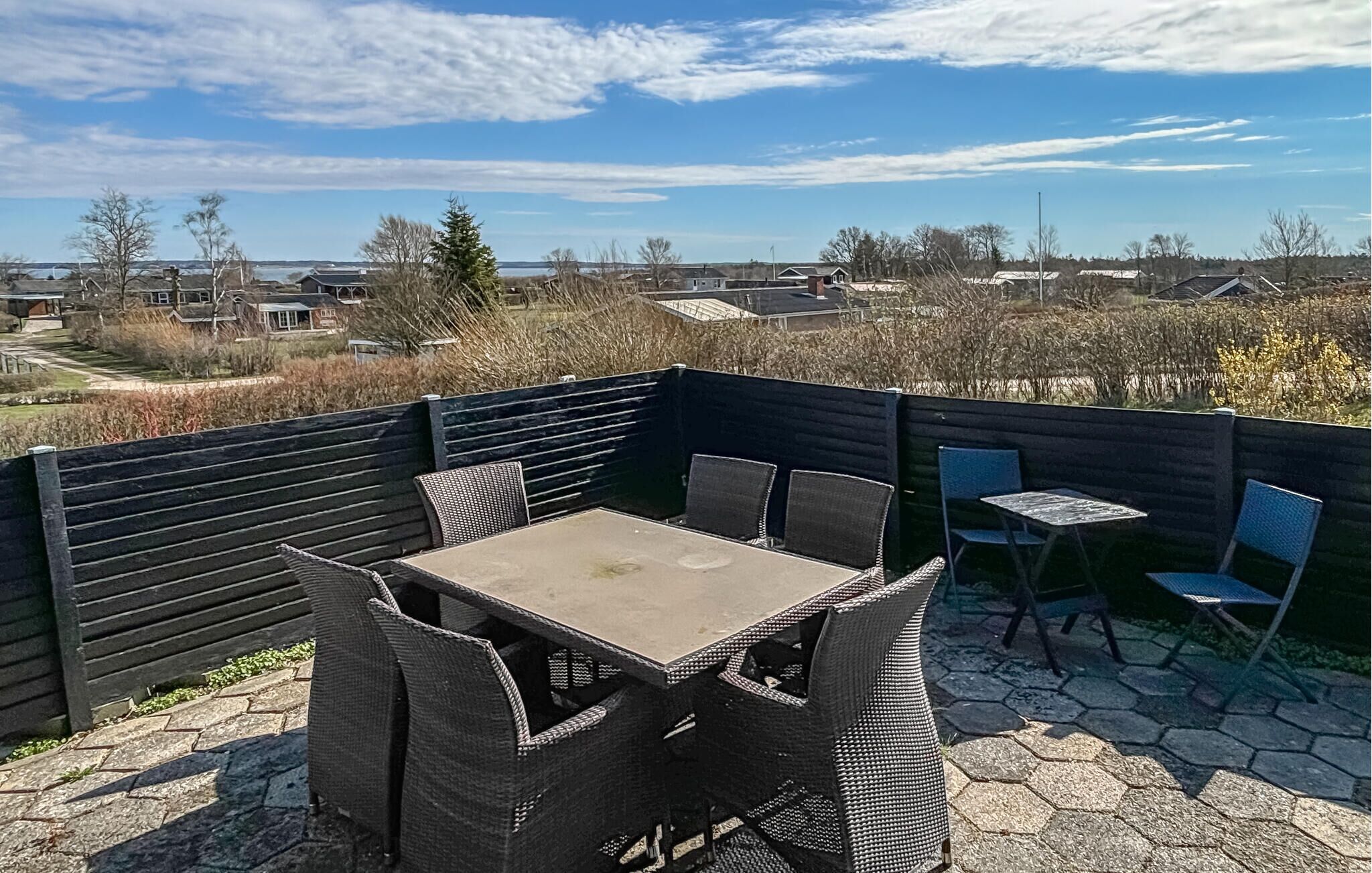 Une terrasse extérieure avec une table et des chaises, une vue sur des maisons au loin et une clôture en bois.