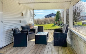 A covered patio with wicker furniture, a grill, and a view of a house and greenery. - 2 bedroom stunning home in Roslev (Roslev)