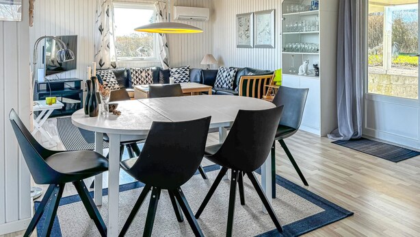A dining area with a round table, black chairs, a patterned sofa, and a cabinet with glassware.