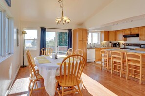Une cuisine spacieuse avec des meubles en bois, une table à manger avec des chaises et une vue sur l’extérieur grâce à de grandes fenêtres.
