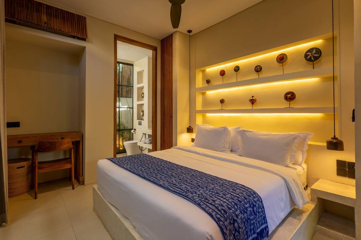 A bedroom with a bed, bedside tables, a desk, and a chair.