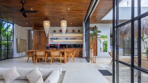 A modern interior with a dining area, kitchen, and large windows. - Aricivillas (Pecatu)